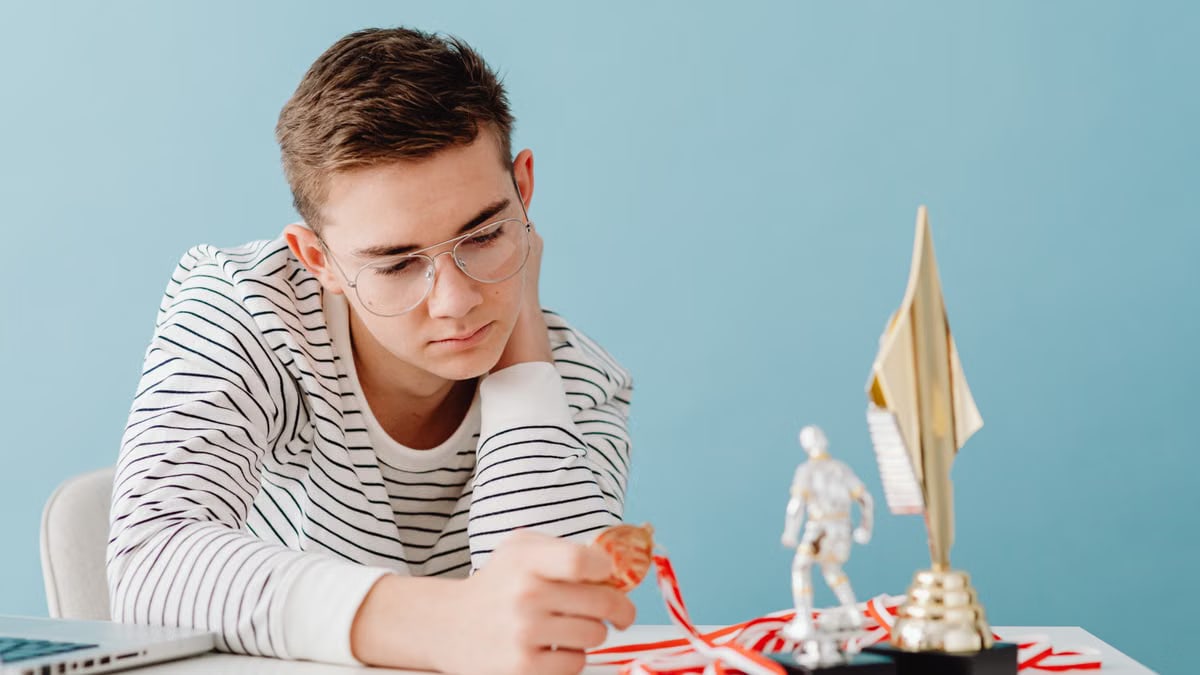 Young man with eyeglasses examines his medals and trophies, reflecting success.